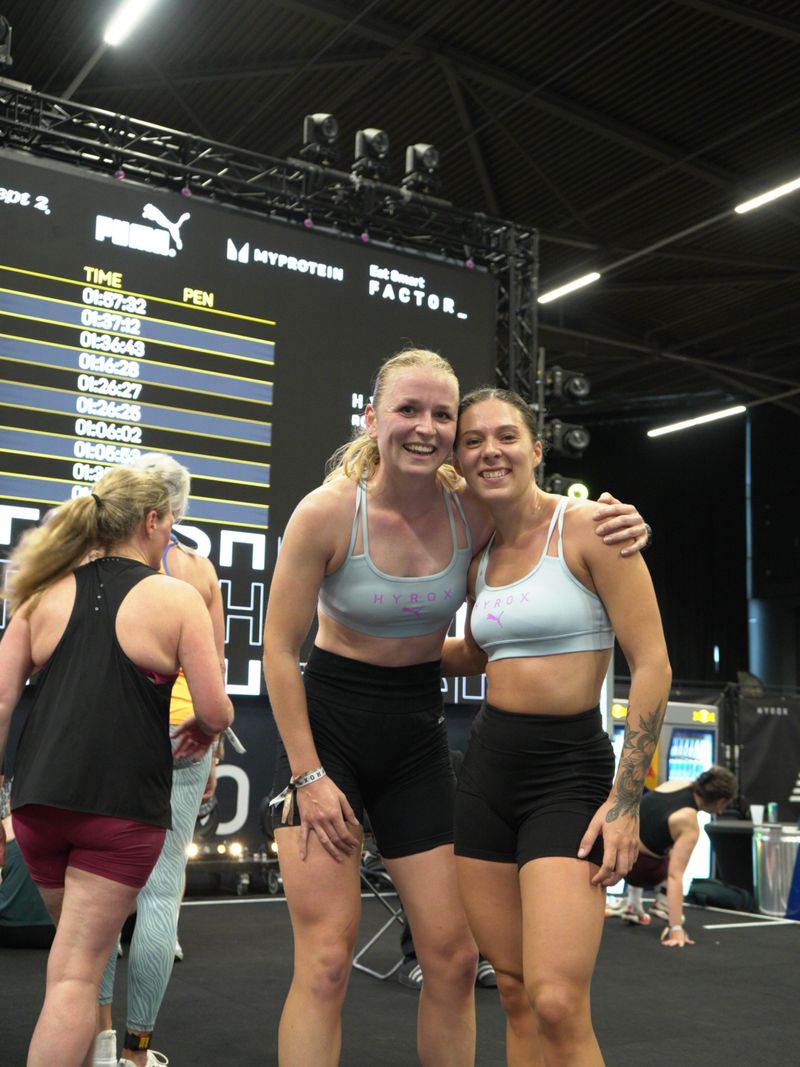 Twee atleten van Momentom voor het scorebord na hun Hyrox race